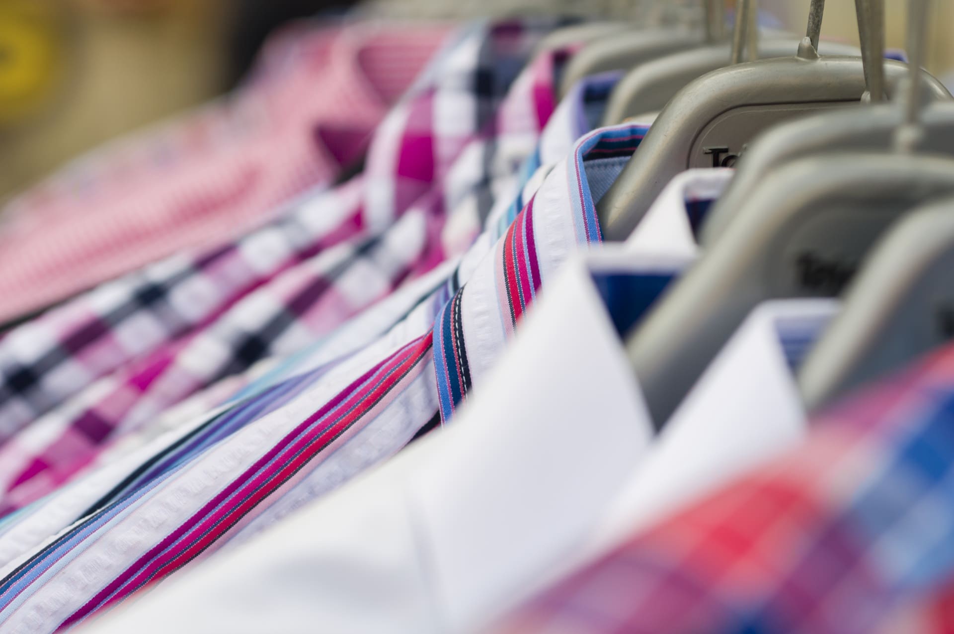 Close-up of several colorful plaid and striped shirts hanging on a clothing rack, arranged neatly side by side.